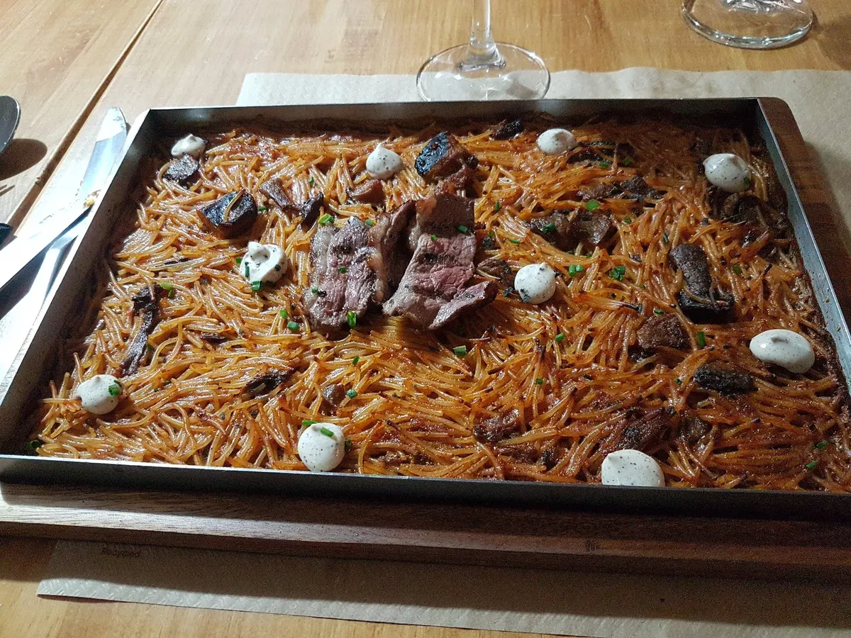 Fideuà en llauna con carne y puntos de salsa sobre la mesa