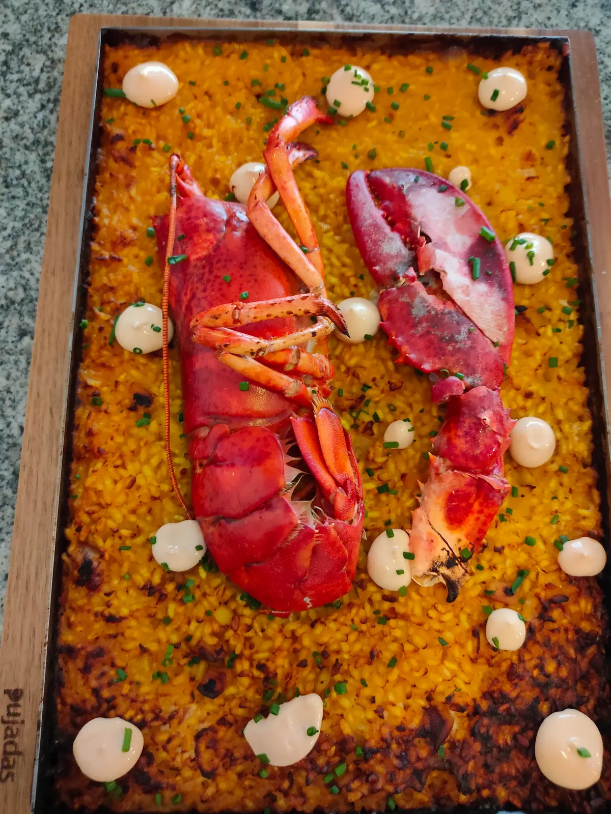 Arroz en llauna con bogavante y puntos de salsa, servido sobre tabla de madera