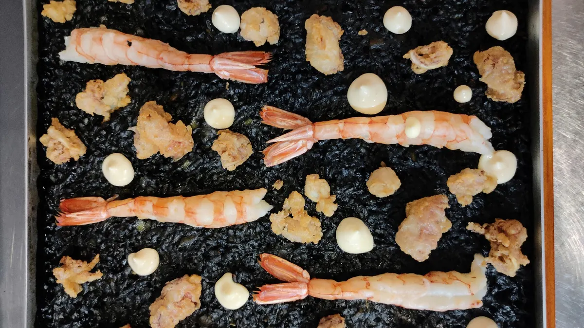 Arroz negro en llauna con gambas, rebozados y puntos de salsa
